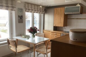 A kitchen with a dining table, chairs, a clock, a television, and a window with curtains. - Holiday apartment with 2 bedrooms (Wyk OT Boldixum \/ Föhr)