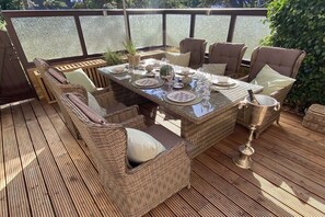 An outdoor dining area with wicker furniture, a glass-top table, and a view of the water. - Holiday apartment with 2 bedrooms (St. Peter-Ording)