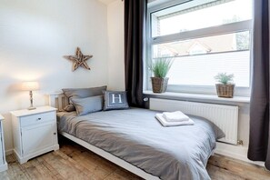 Une chambre avec un lit simple, une table de chevet, une décoration en forme d’étoile, une fenêtre avec des plantes et un radiateur.