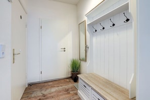 Ein Flur mit einer weißen Tür, einem Blumentopf, einem Spiegel und einer hölzernen Bank mit Haken.
