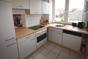 A compact kitchen with white cabinets, a black stove, and a window providing a view of the outside. - Holiday apartment with 2 bedrooms (Kühlungsborn)