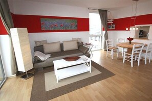 A modern living room with a sofa, coffee table, and dining area with chairs. - Holiday apartment with 2 bedrooms (Kühlungsborn)