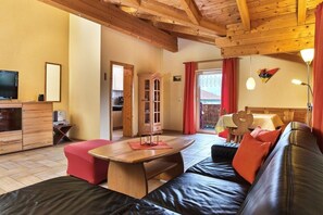 Een gezellige woonkamer met een houten plafond, een bank, een eettafel en een televisie.