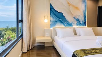 A hotel room with a large bed, a bedside table, a nightstand, a wall-mounted lamp, and a view of the sea.