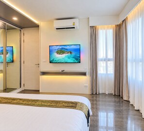 Habitació d'hotel amb llit, televisió de pantalla plana penjada a la paret, aparell d'aire condicionat i una finestra gran amb cortines.