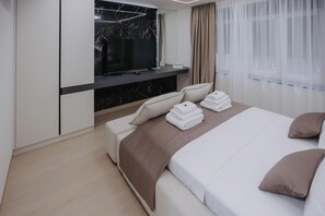 A modern hotel room with a flat-screen TV mounted above a marble fireplace, a bed with neatly folded towels, and a large window with sheer curtains. - Premium Smart-Home Spa Residence Near Banja Luka Centre (Banja Luka)