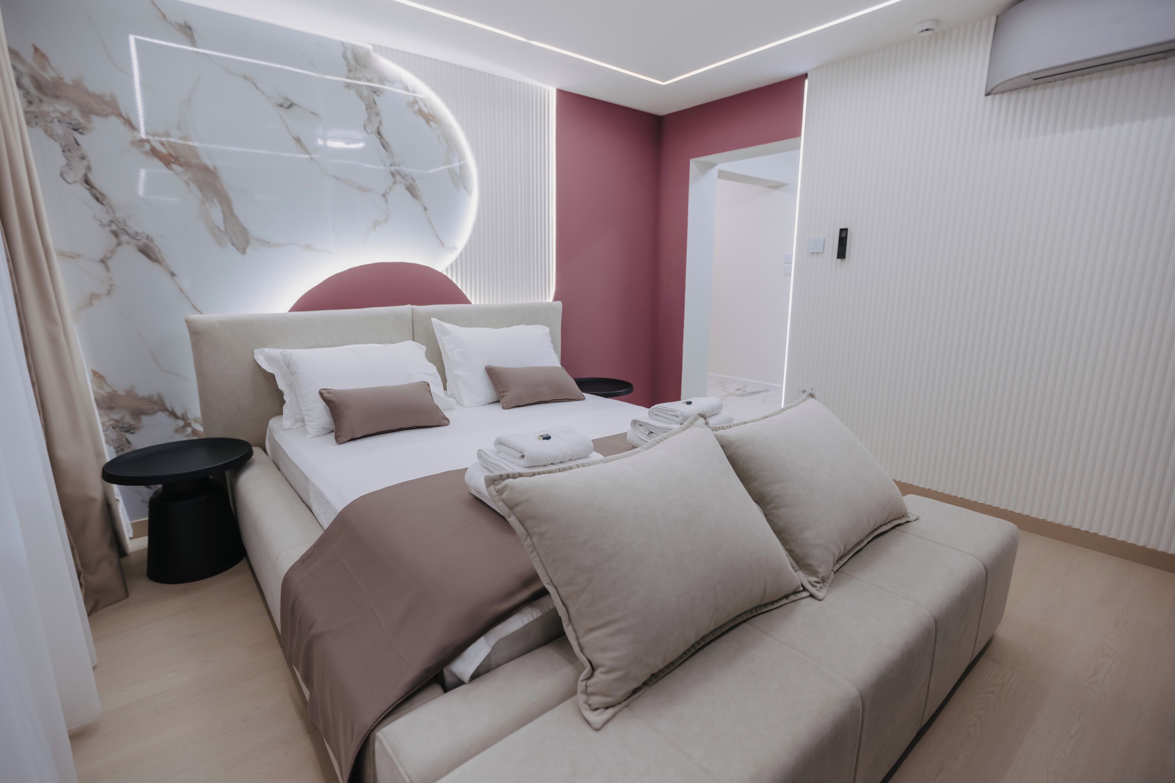 Un dormitorio moderno con cama, mesitas de noche, un sofá y una pared de mármol.