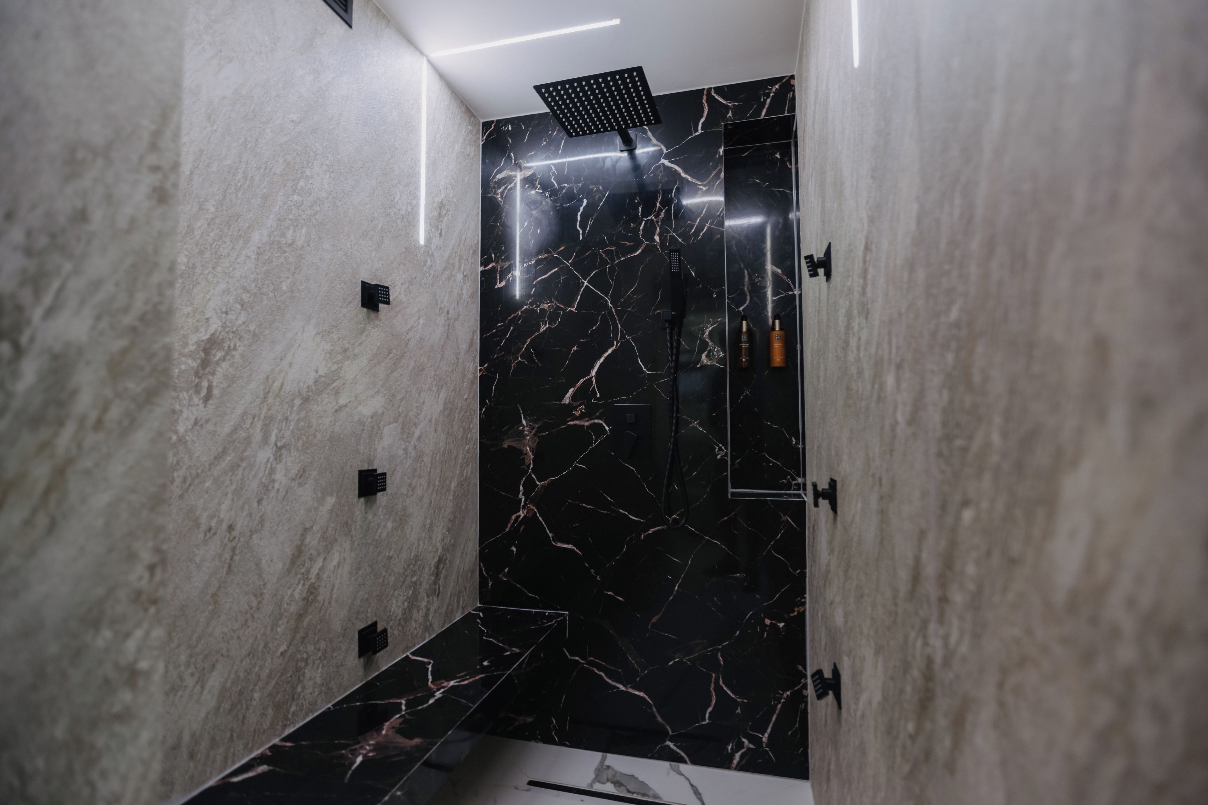 Een moderne badkamer met een douchecabine van zwart marmer en een vloer van wit marmer.