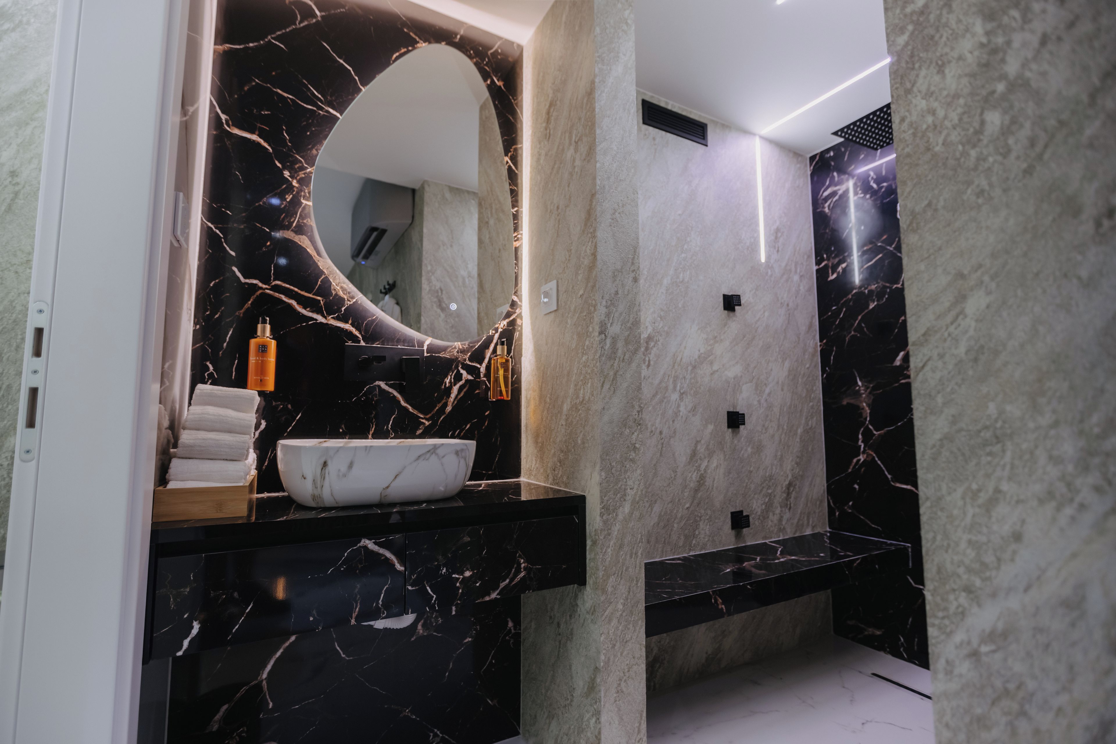 Un baño moderno con tocador de mármol, un espejo grande y un lavamanos blanco.