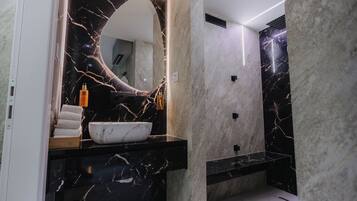 Un baño moderno con tocador de mármol, un espejo grande y un lavamanos blanco.