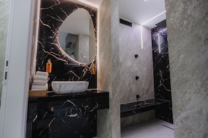 Un baño moderno con tocador de mármol, un espejo grande y un lavamanos blanco.