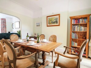 A dining room with a wooden table set for four, surrounded by chairs. A bookshelf filled with books is to the right. - Fernleigh (Margate)