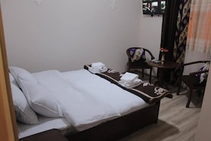 Een hotelkamer met een bed, twee stoelen, een tafeltje en een raam met gordijnen.