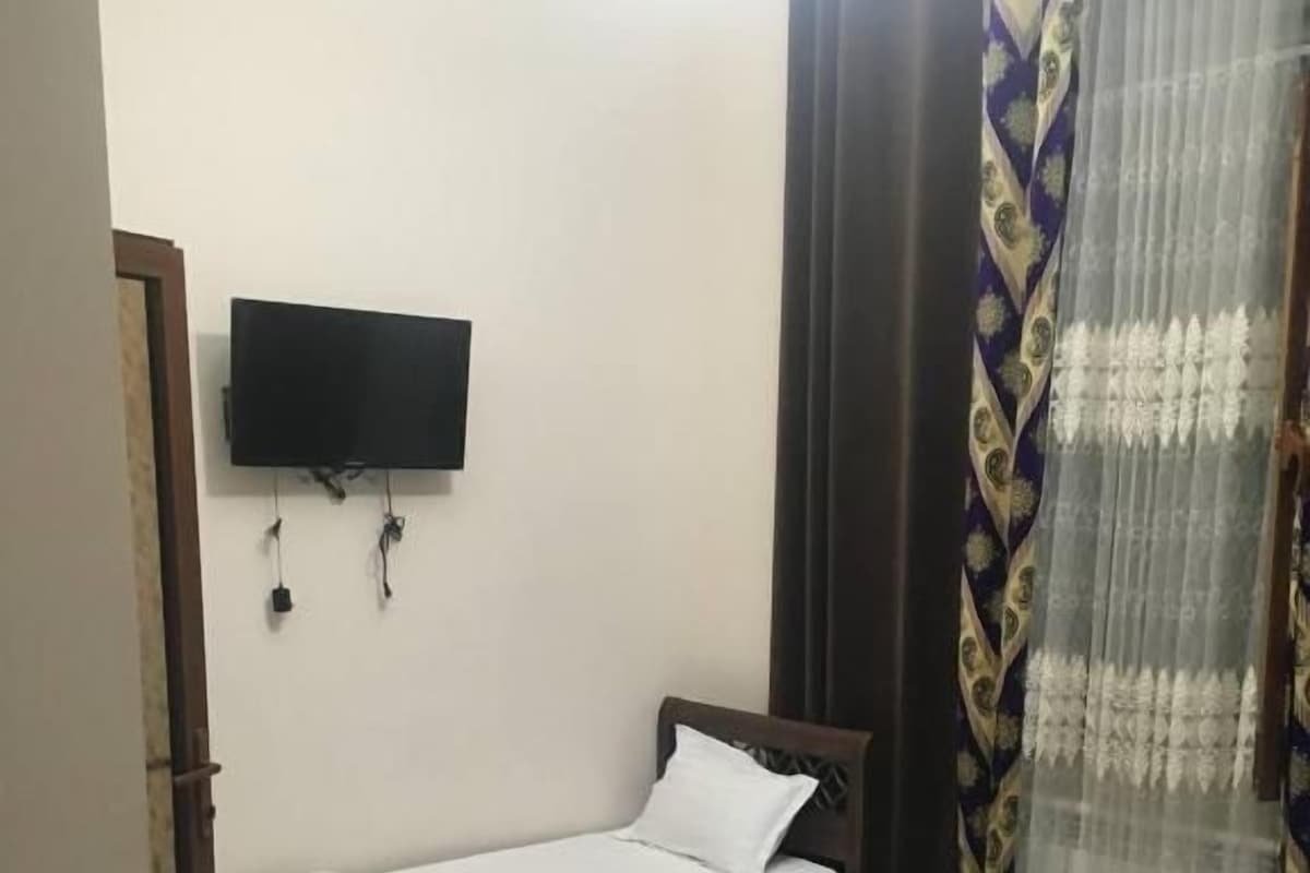 Een kamer met twee eenpersoonsbedden, een wandgemonteerde flatscreen-tv en een raam met decoratieve gordijnen.