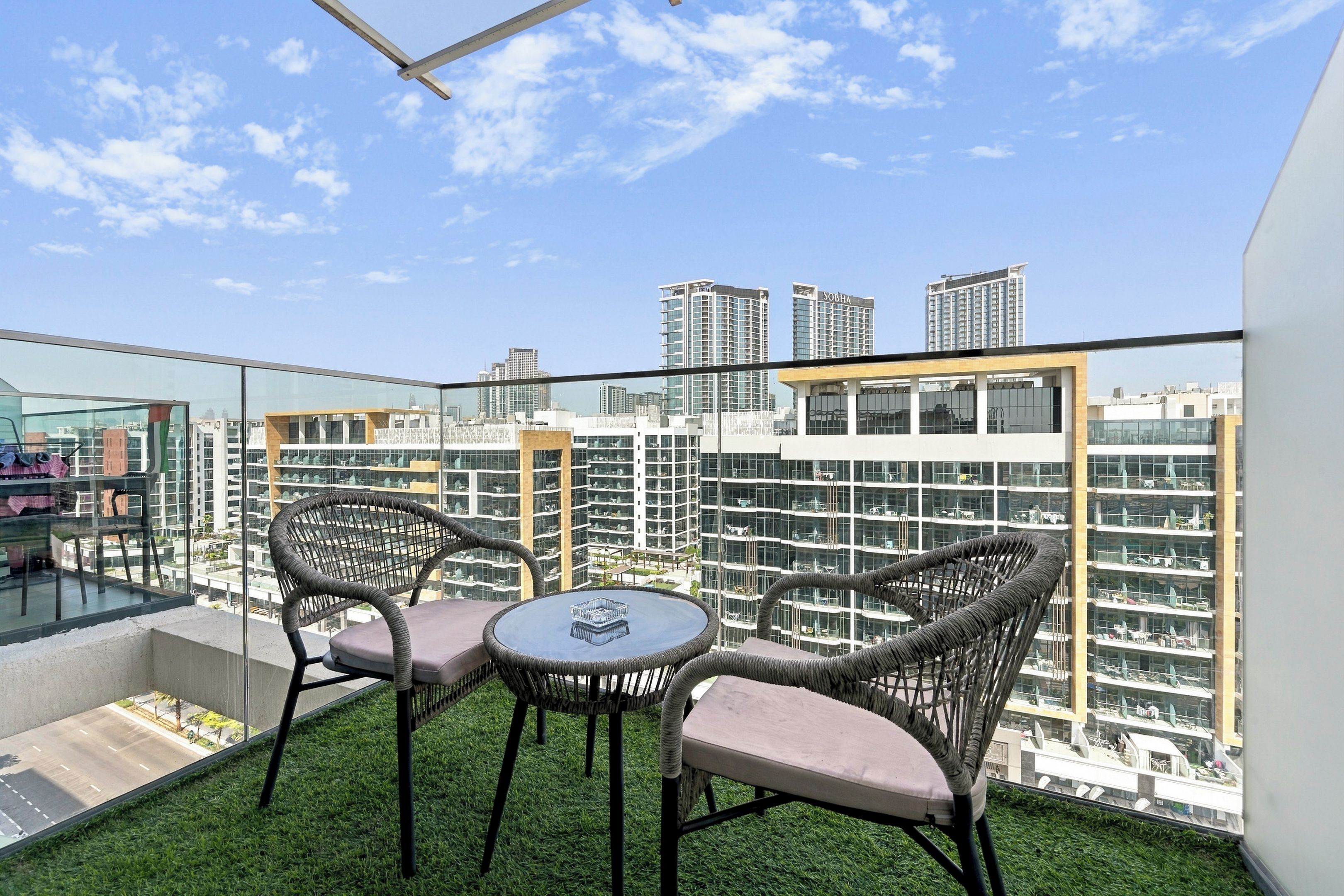 Un balcone con due sedie in vimini e un piccolo tavolo rotondo, con vista su un panorama urbano ricco di grattacieli.