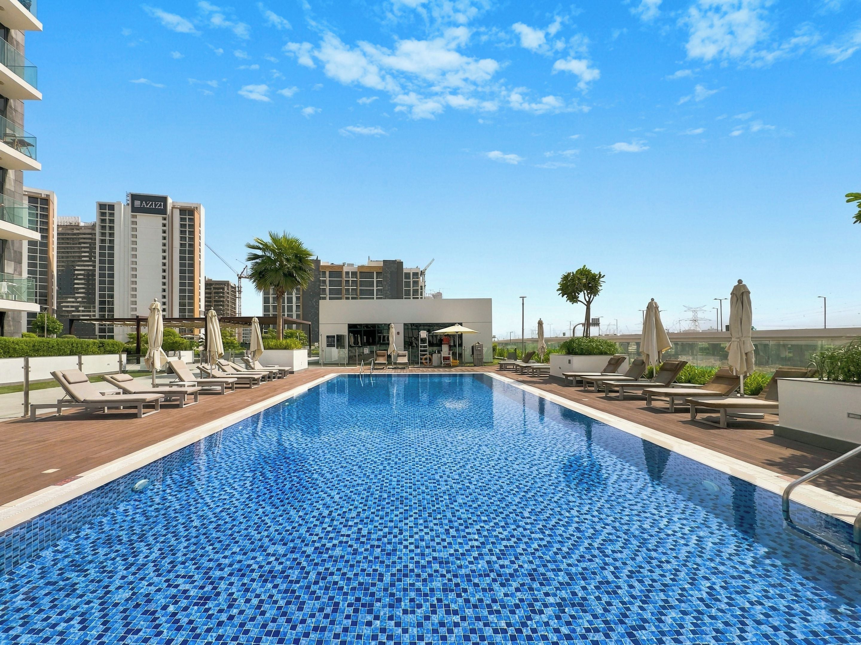 Una piscina sul tetto con lettini e ombrelloni, circondata da edifici moderni e un cielo sereno.