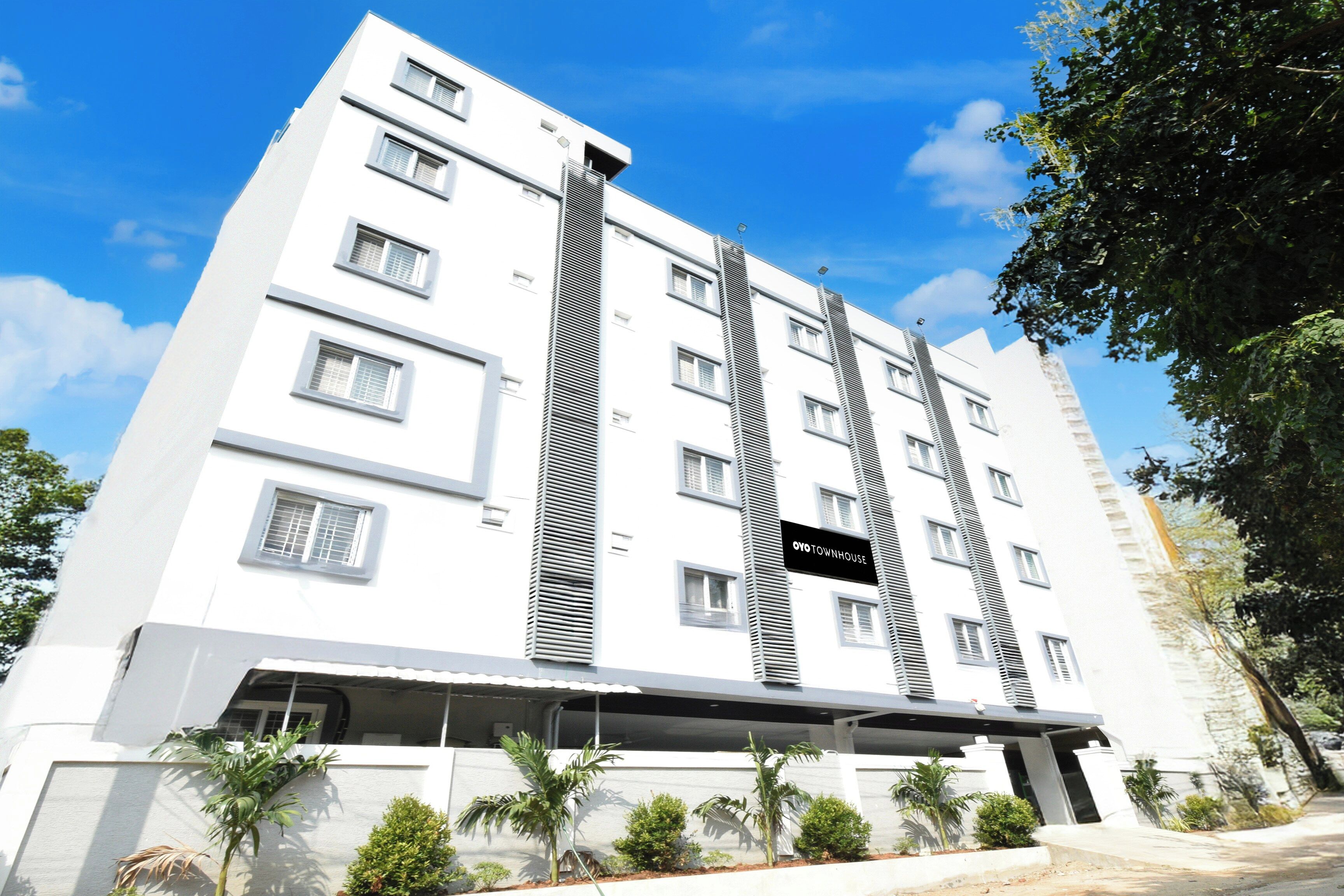 Un edificio a più piani con un design architettonico moderno, caratterizzato da un elemento verticale distintivo e un cartello con la scritta 'OYO TOWNHOUSE'.