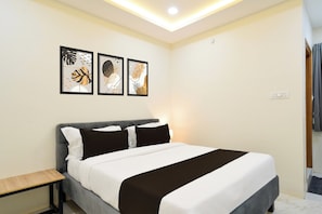 Una cama con cabecera gris, ropa de cama blanca y negra, y tres cuadros en la pared.