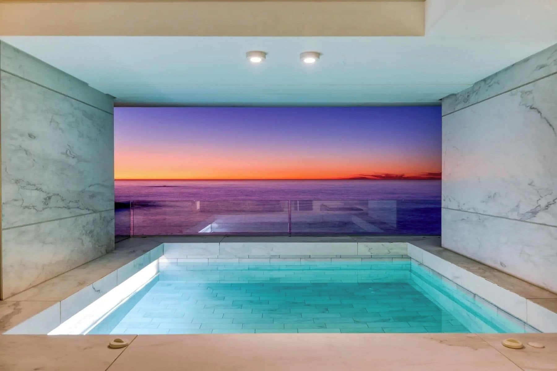 Piscina coberta moderna com vista para o pôr do sol sobre o oceano.