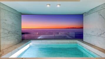 Piscina coberta moderna com vista para o pôr do sol sobre o oceano.