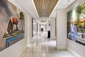 A hallway with a modern design, featuring a wooden ceiling and two large wall paintings depicting nature scenes. - Aurum Presidential Palace (Cape Town)