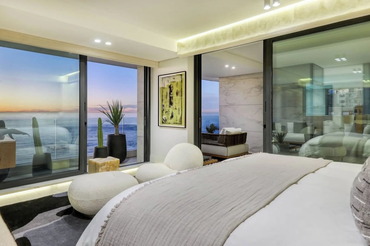 Quarto moderno com uma cama grande, vista para o oceano e chuveiro em vidro.