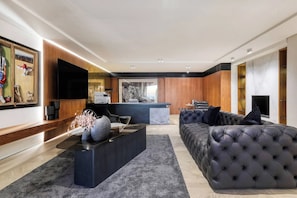 Uma sala de estar moderna com um sofá preto grande, uma mesa de centro de vidro e uma TV de tela plana fixada na parede.