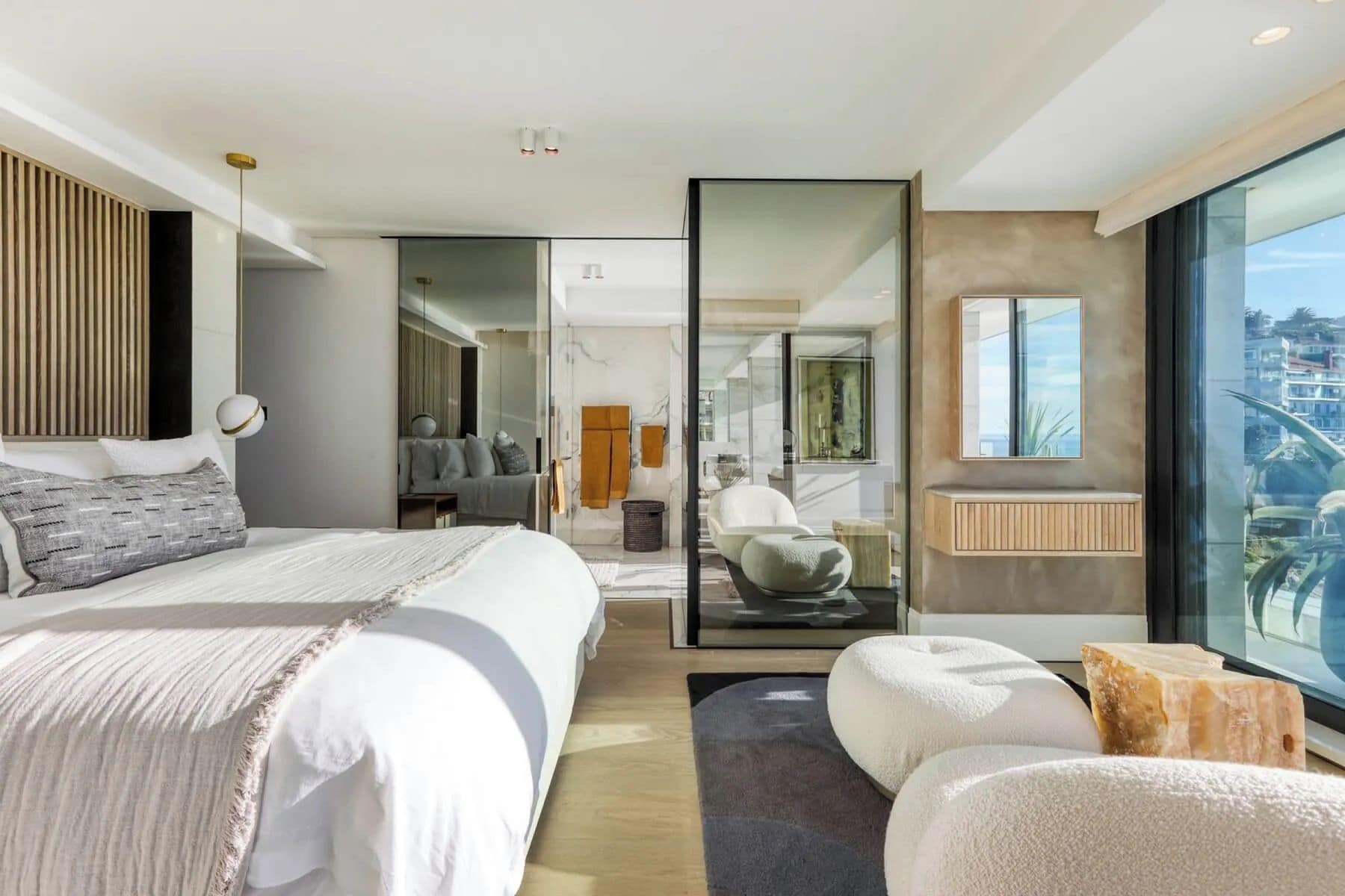 Quarto de hotel moderno com cama grande, área de estar, divisória de vidro e vista para a cidade.