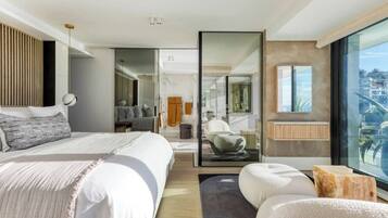 Quarto de hotel moderno com cama grande, área de estar, divisória de vidro e vista para a cidade.