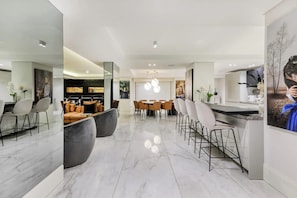 A modern kitchen with a central island, dining area with chairs, and a bar area with stools. - Aurum Presidential Palace (Cape Town)