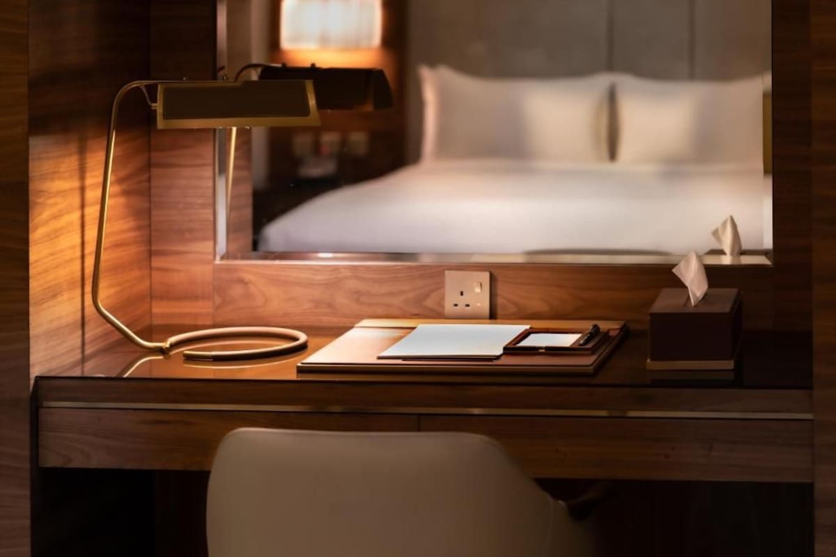 Ein Hotelzimmer mit Holzschreibtisch, Lampe, Bett und Nachttisch mit Taschentuchbox.