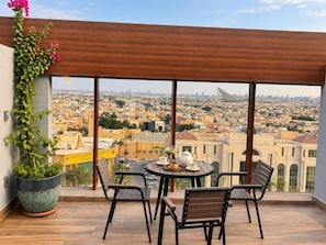 Ein Balkon mit Blick auf eine Stadtansicht, einem Tisch mit Stühlen und einer Kübelpflanze.