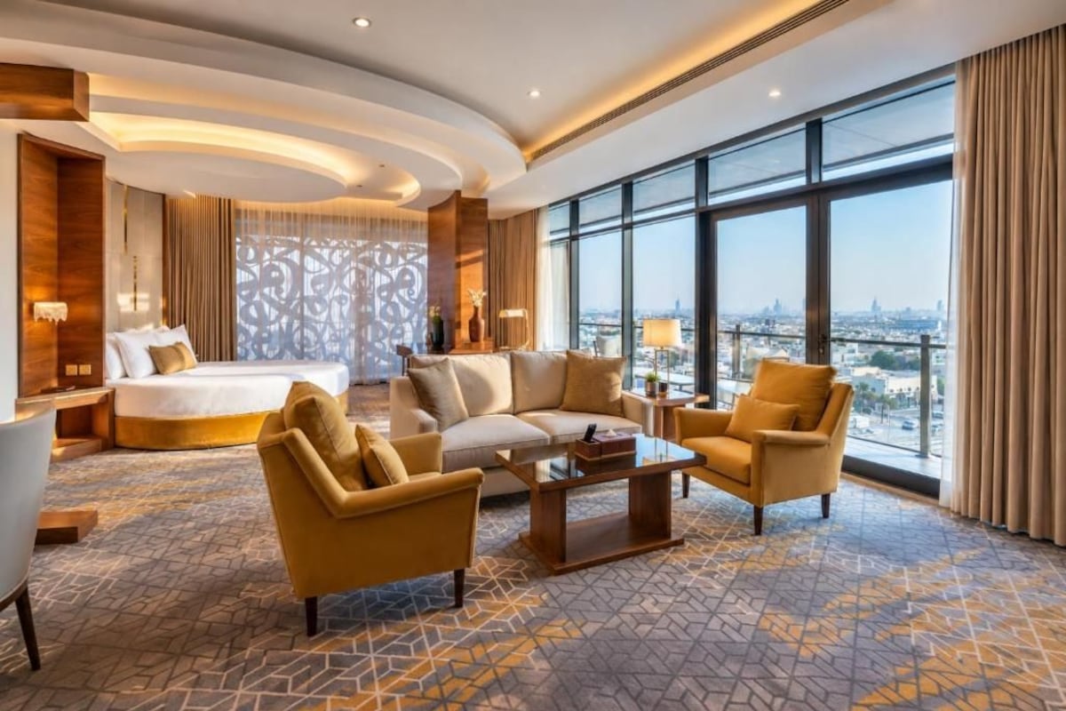 Ein Hotelzimmer mit einem Bett, zwei Sofas, einem Couchtisch und einem großen Fenster mit Blick auf die Stadt.