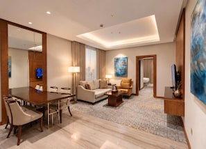 A hotel room with a dining table, sofa, and armchairs, a large mirror, and artwork on the walls. - Otero Hotel and Suites - Riyadh (Riyadh)