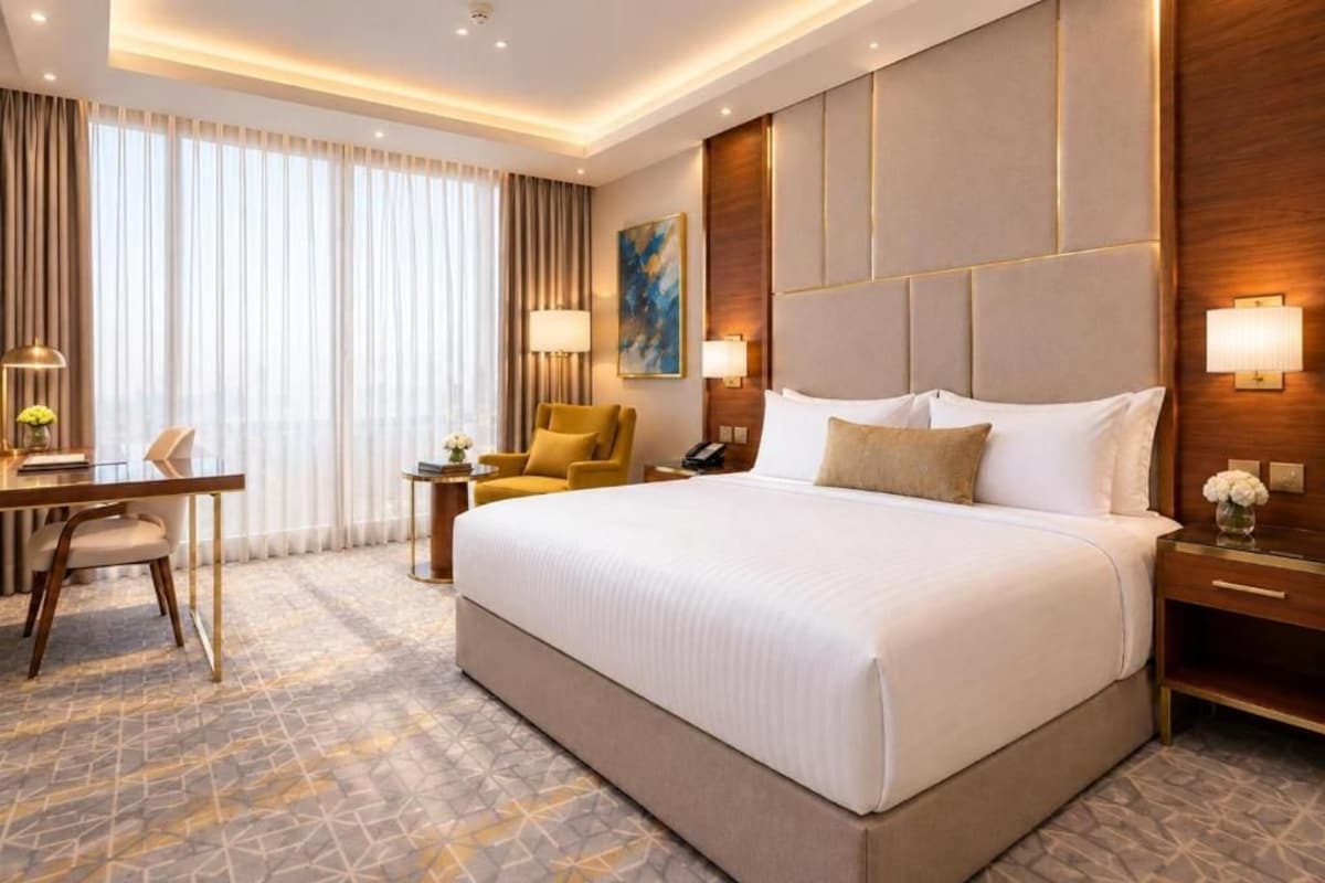 Ein Hotelzimmer mit einem großen Bett, einem Schreibtisch mit Stuhl, einem kleinen Tisch und einer Lampe.