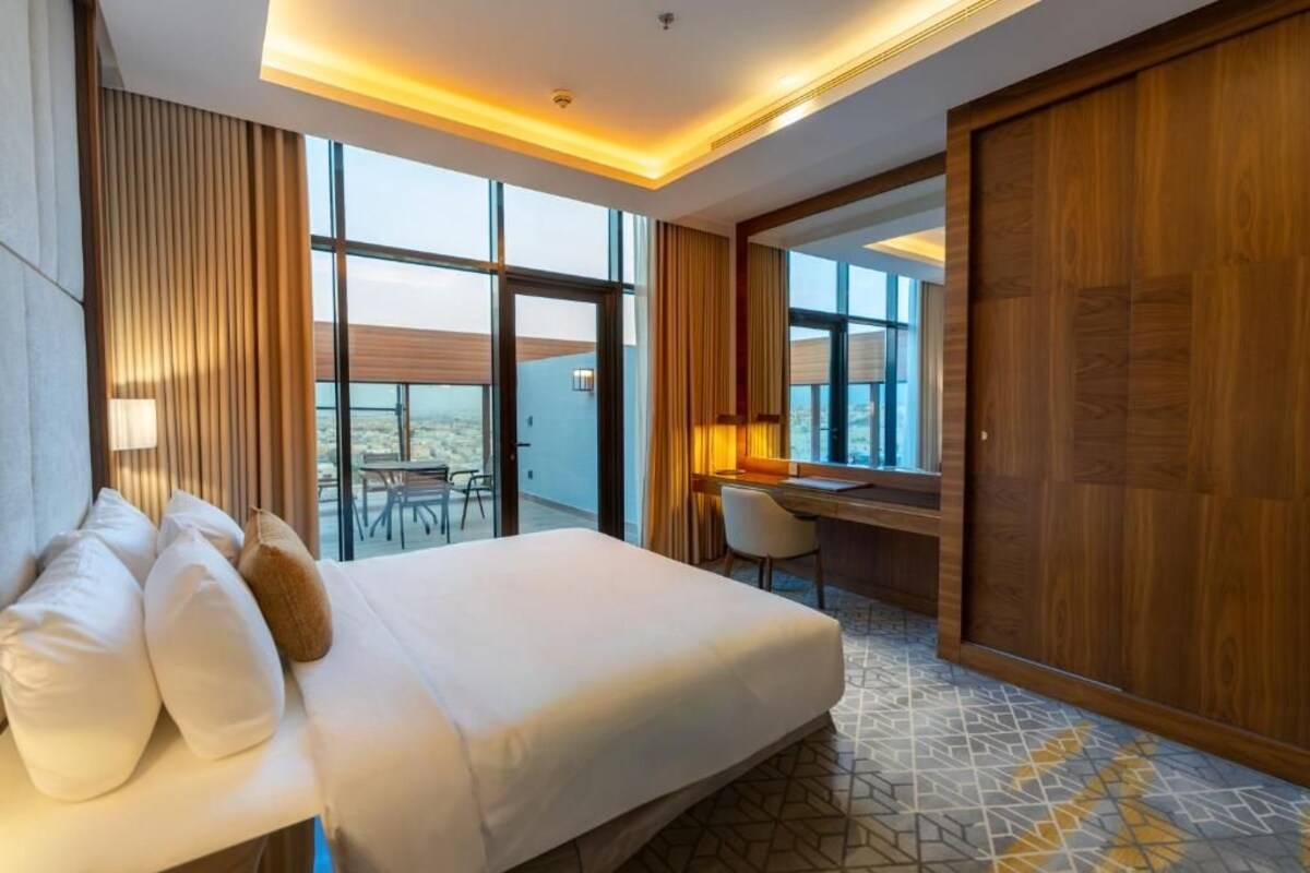 A hotel room with a bed, a desk, and a view of the city.
