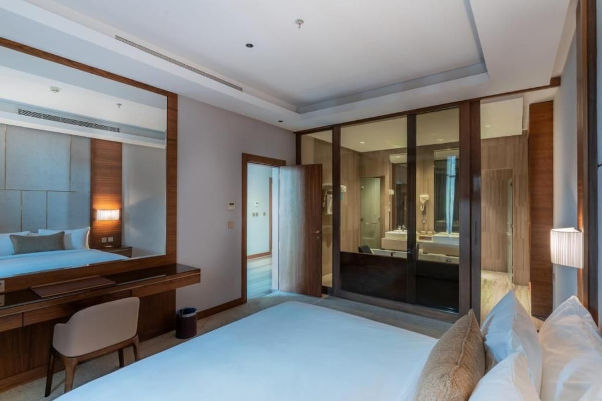 Ein modernes Hotelzimmer mit einem großen Bett, einem Schreibtisch, einem Stuhl und einer Schiebetür zu einem Badezimmer.