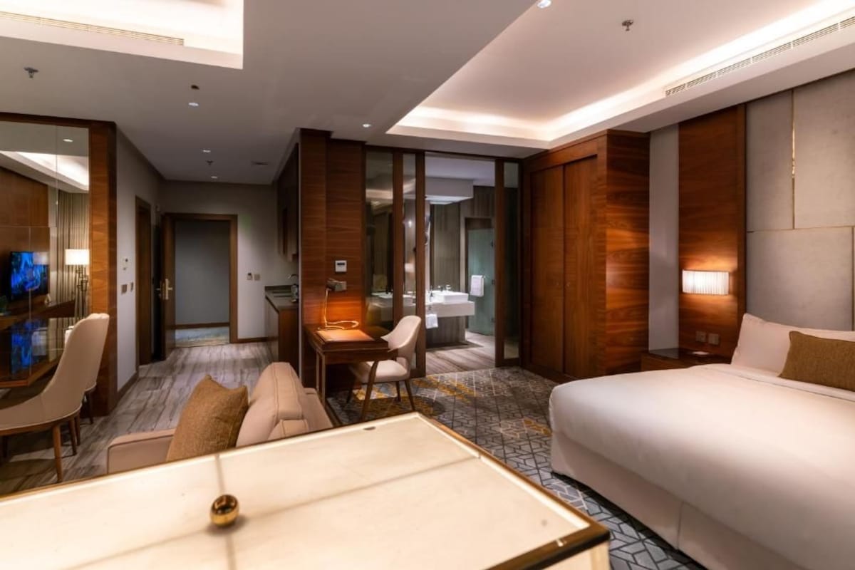Ein Hotelzimmer mit Bett, Schreibtisch, Stuhl, Sofa und Fernseher.