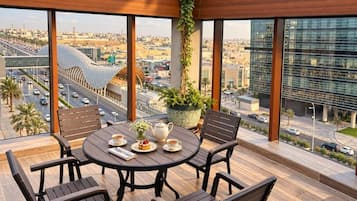 A round table with chairs on a balcony, overlooking a cityscape with modern buildings and a curved structure.
