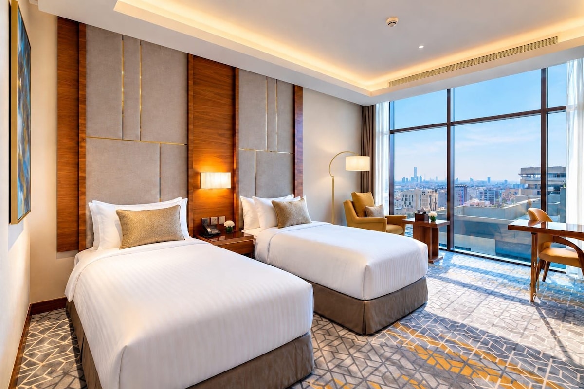 A hotel room with two beds, a city view, a desk, and a chair.