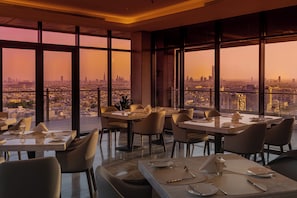 A restaurant with tables set for dining, large windows offering a city view, and a modern interior design. - Otero Hotel and Suites - Riyadh (Riyadh)