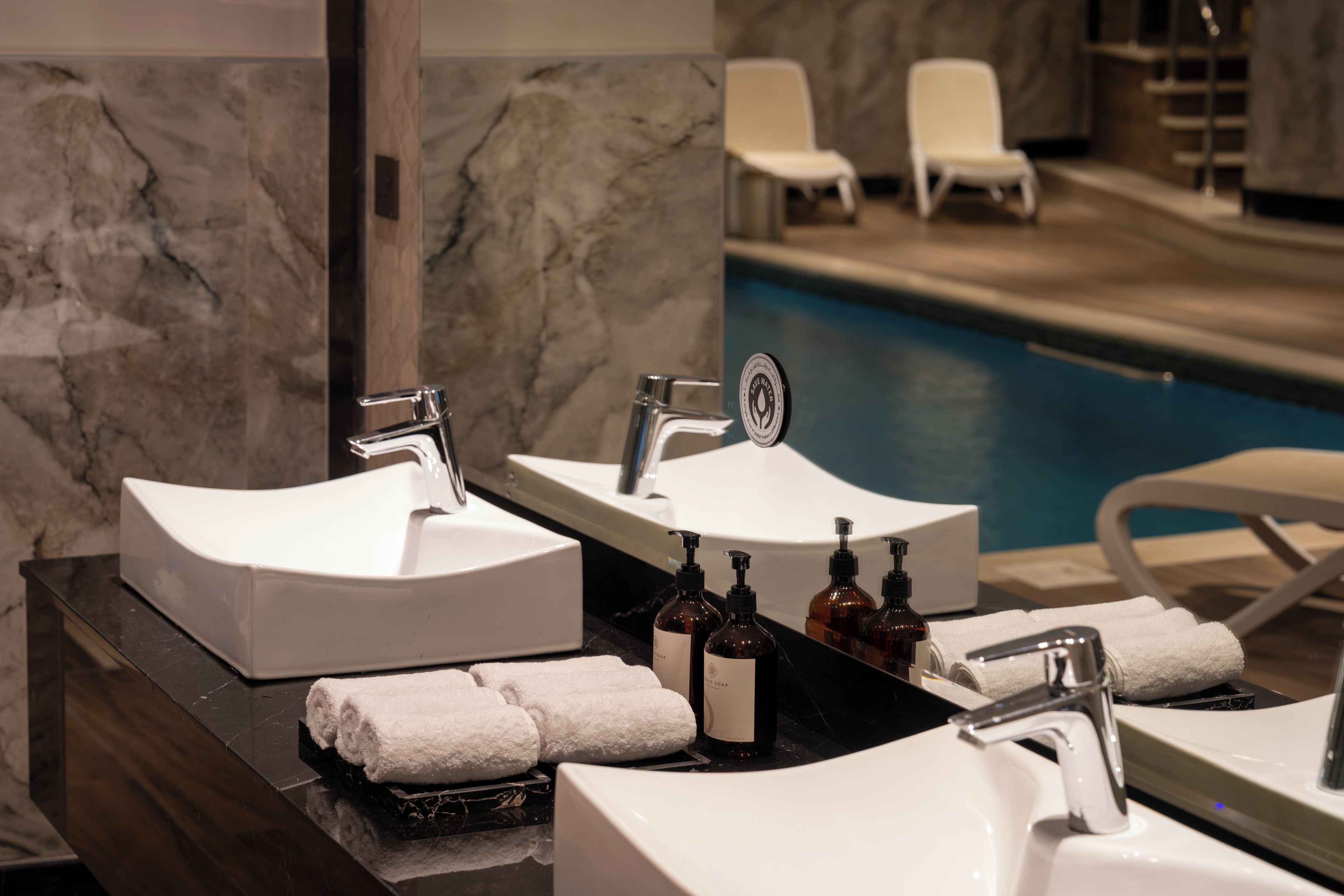 A bathroom with two sinks, a mirror, and a pool area in the background.