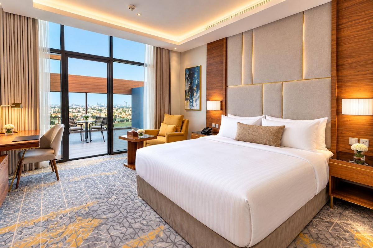 A hotel room with a large bed, a desk, a chair, a table, and a view of the city.