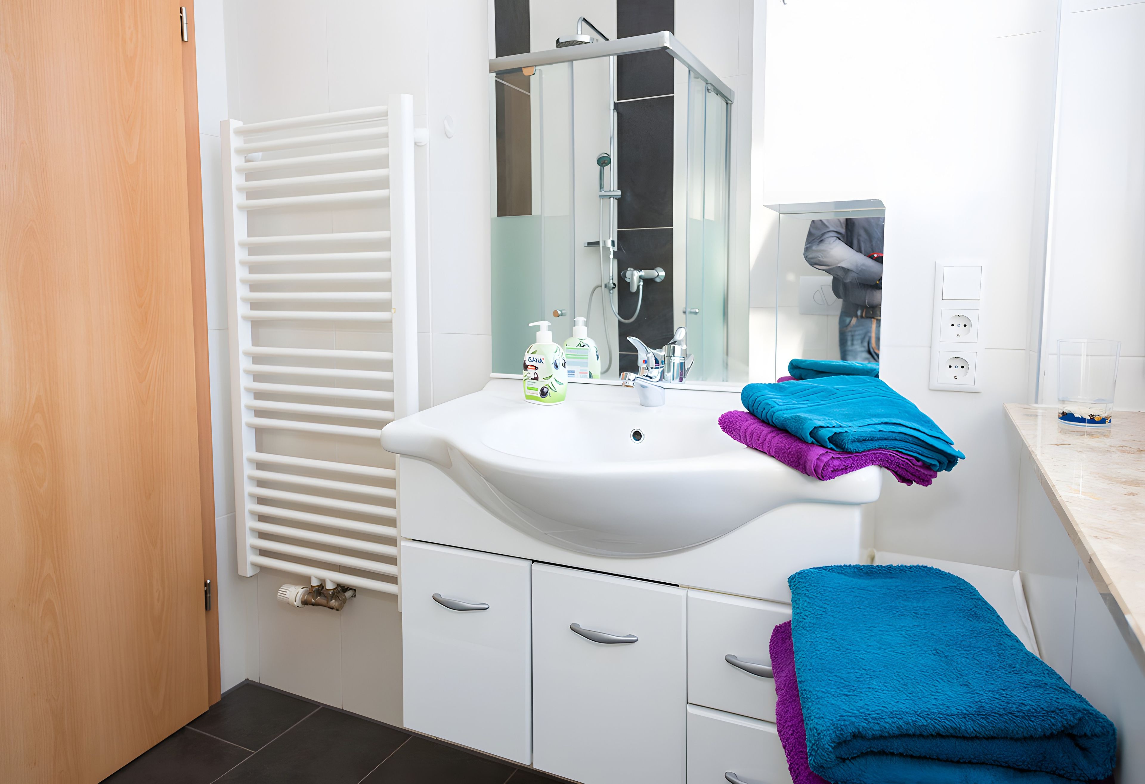 Een moderne badkamer met een wit wastafelmeubel, een douchecabine van glas en een handdoekrek met opgevouwen handdoeken.