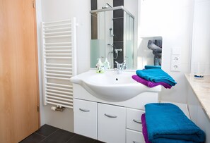 Een moderne badkamer met een wit wastafelmeubel, een douchecabine van glas en een handdoekrek met opgevouwen handdoeken.