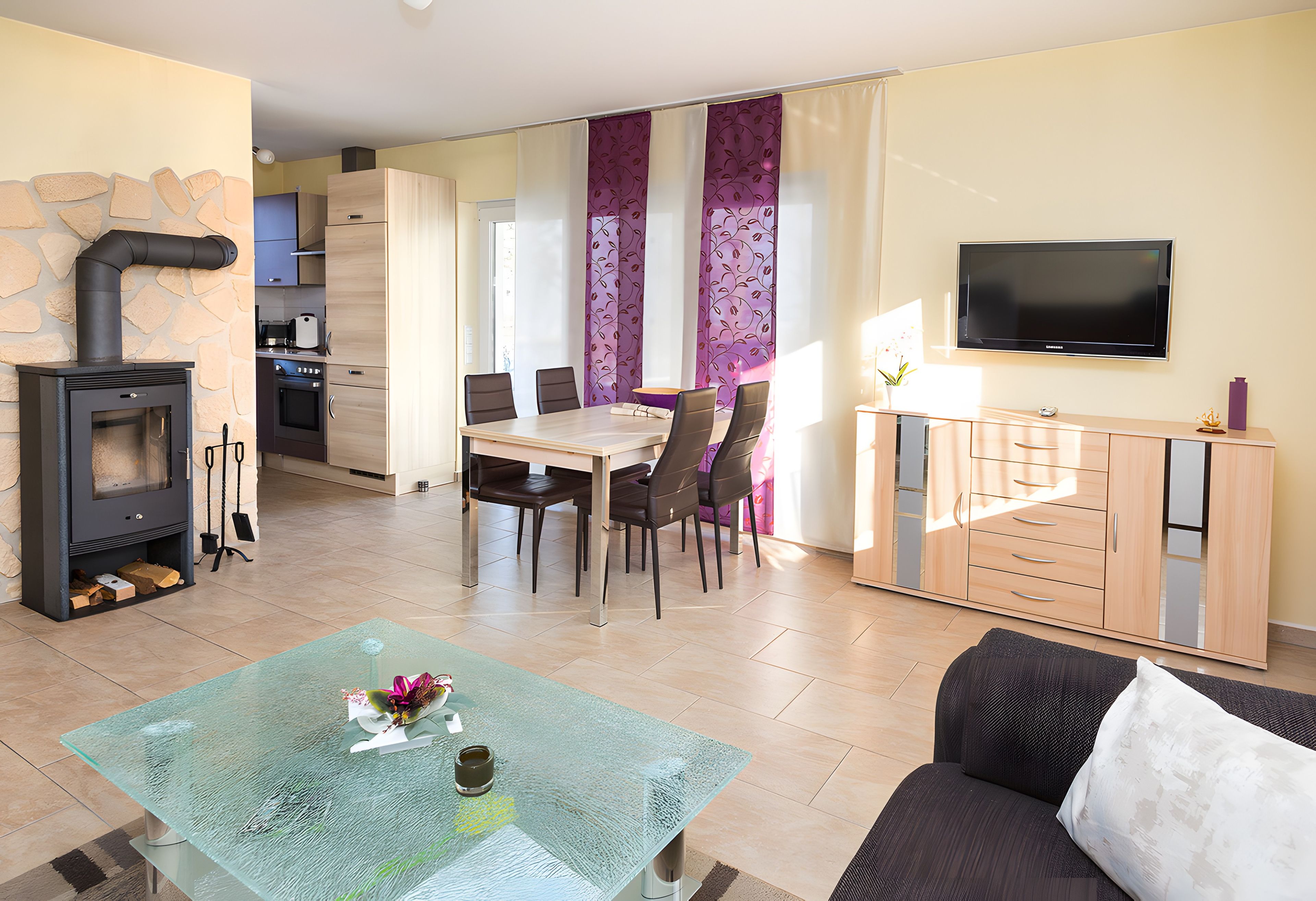 Een woonkamer met een glazen salontafel, een bank, een televisie, een open haard en een eethoek met stoelen en een tafel.