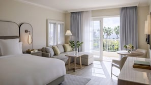 Ein Hotelzimmer mit Bett, einer Couch, einem kleinen Tisch, einem Sessel und einem Balkon mit Vorhängen.