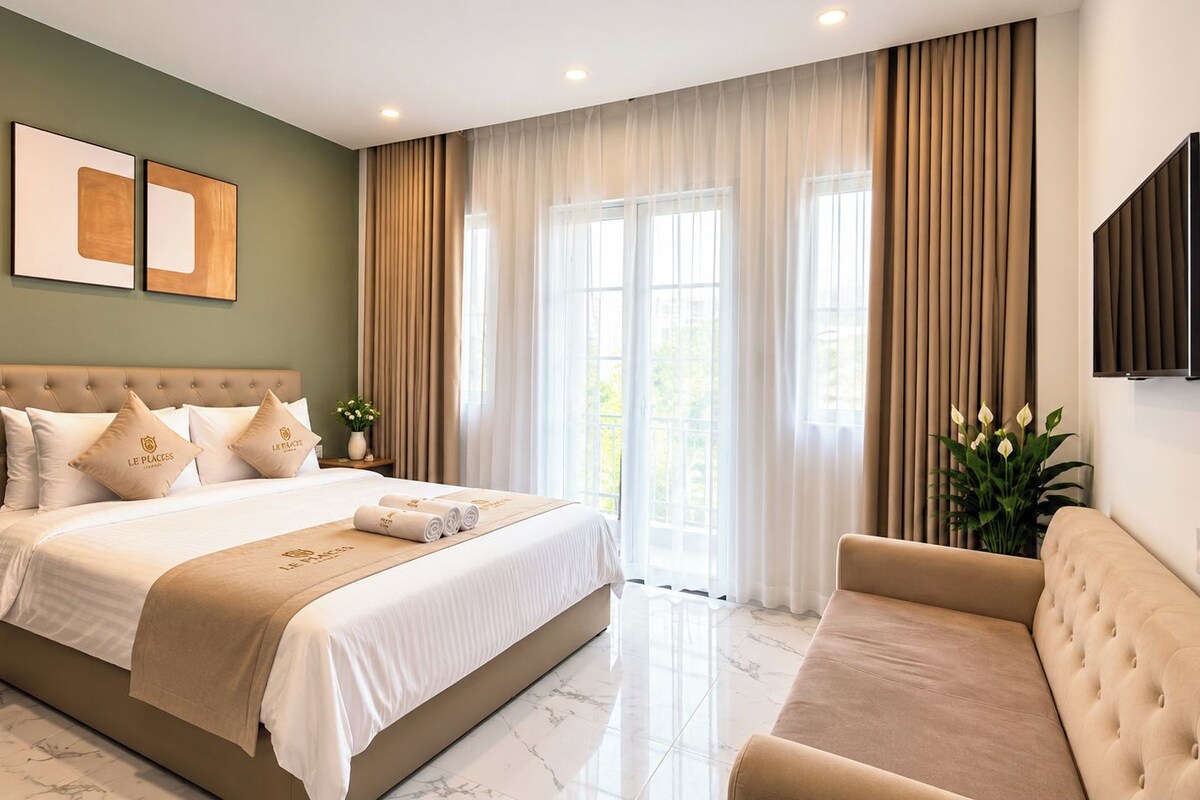 A hotel room with a large bed, a sofa, a flat-screen TV, and a window with curtains.