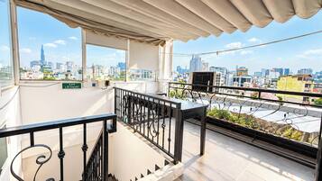 Ein Balkon mit Metallgeländer, einem Tisch und Blick auf eine Stadtlandschaft, einschließlich eines hohen Gebäudes.