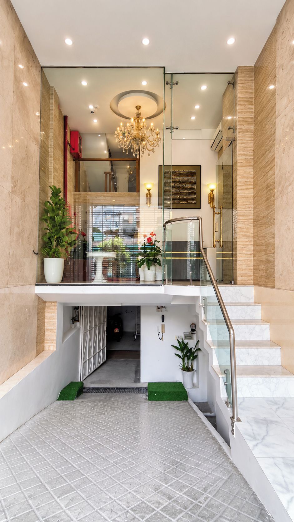 Un hall d’hôtel moderne avec un escalier en marbre, un lustre et des plantes en pot.